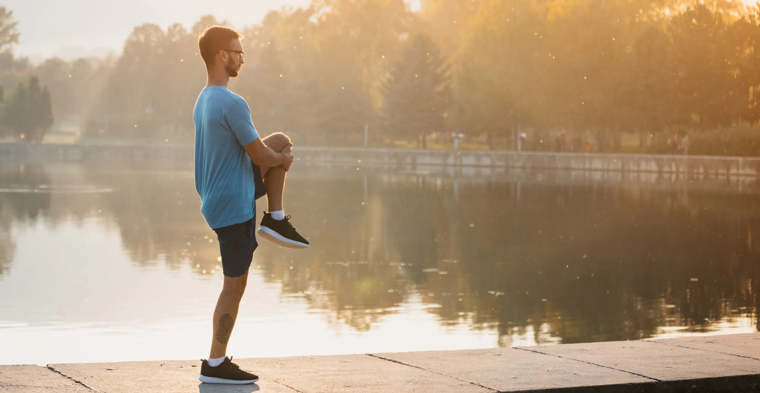 Young man in sportswear stretching by the lake in a city park. R