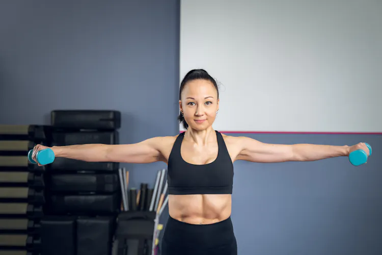 Front view of an Asian woman performing a side lateral raise exe